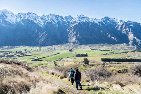 Two people walking a track with mountains and grass land in the background