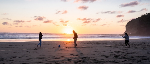 Three people playing with a ball on a beach at sunset