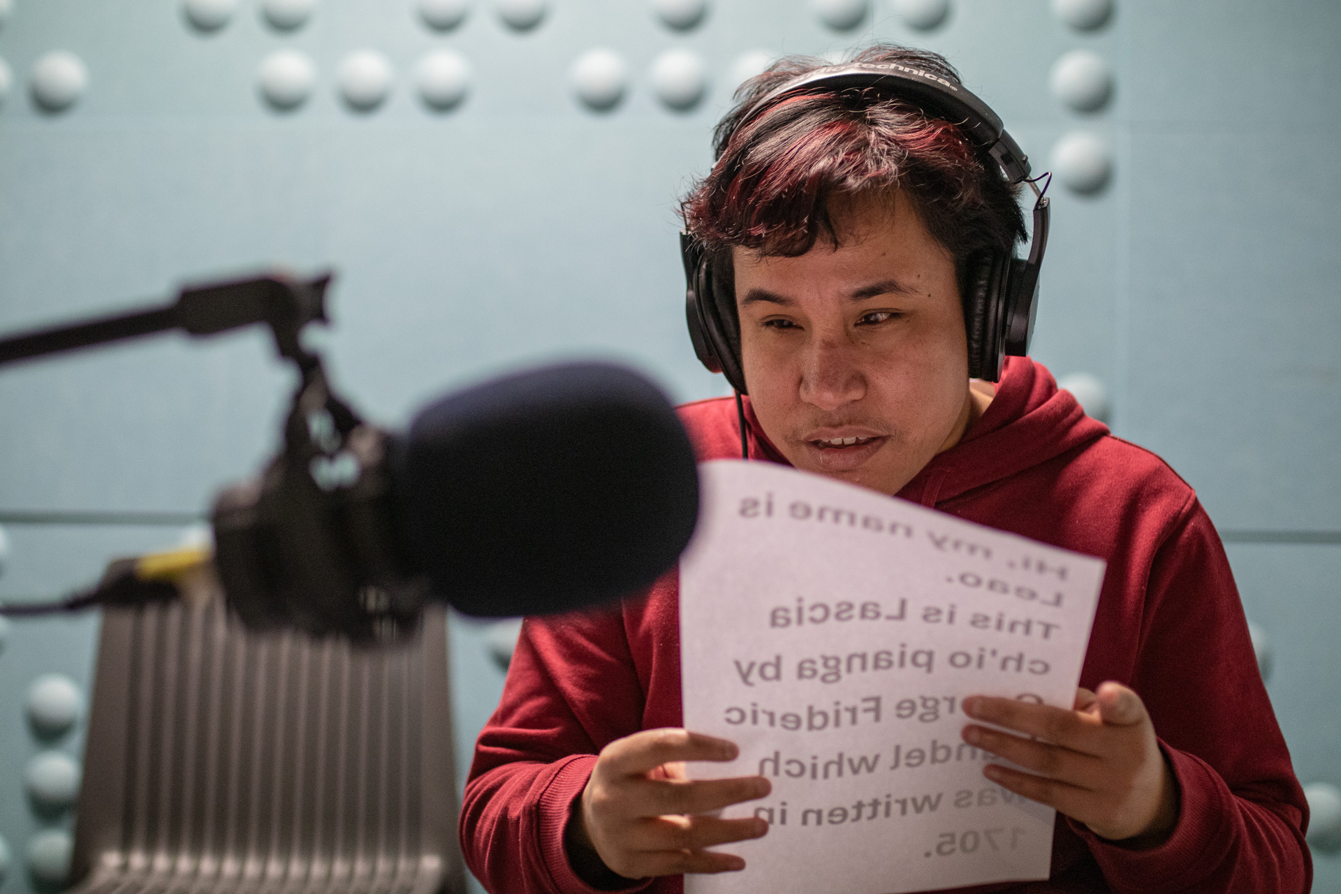 Person with headphones on in front of a microphone reading a script.