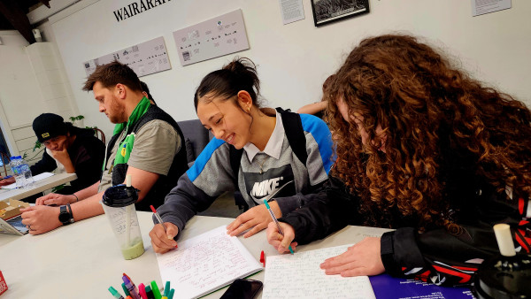 Four rangatahi at Puāwai Pūrau STEMM Academy at a desk writing 