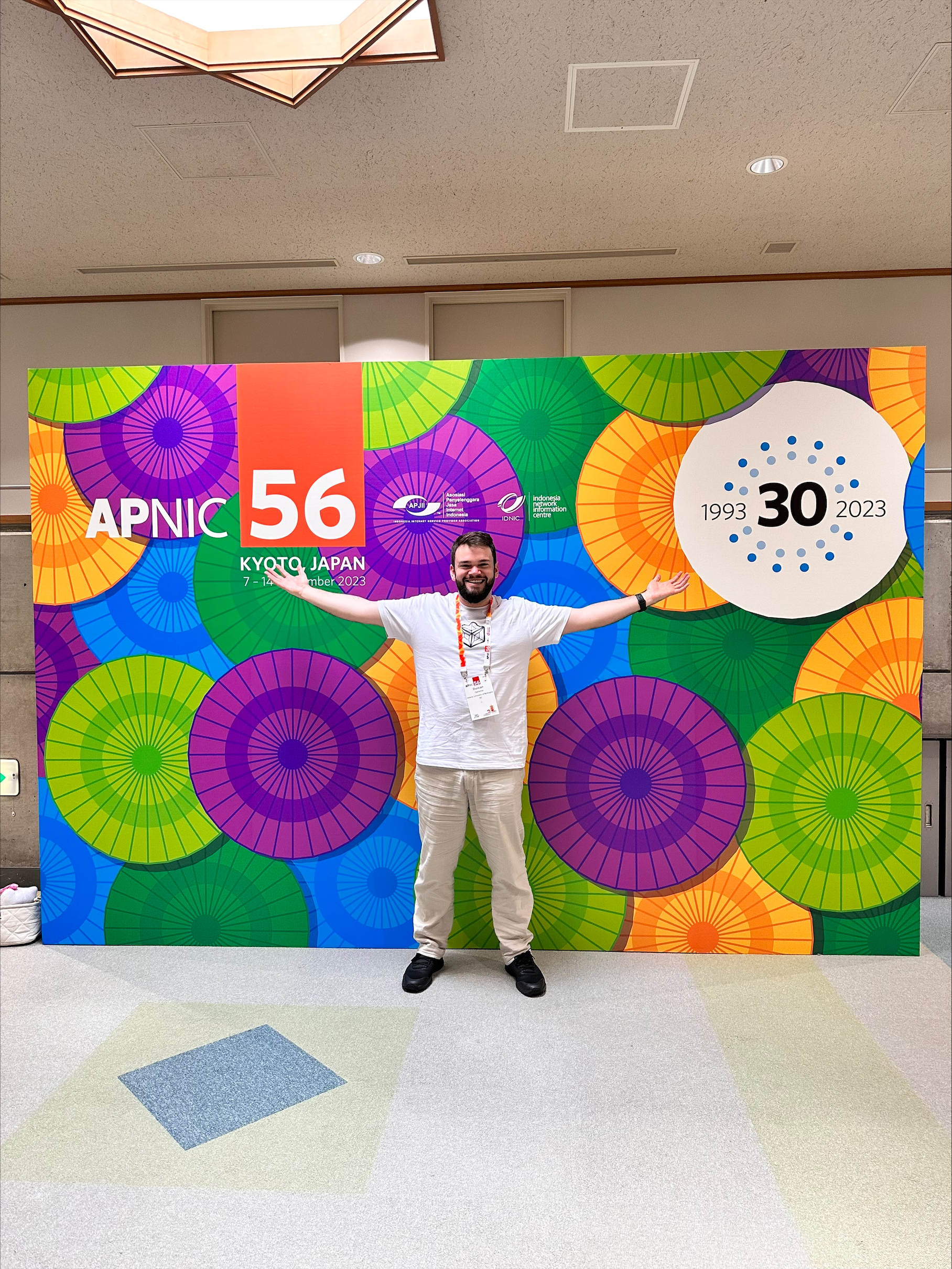 A man named Duncan Cameron posing with arms out on front of a colourful wall