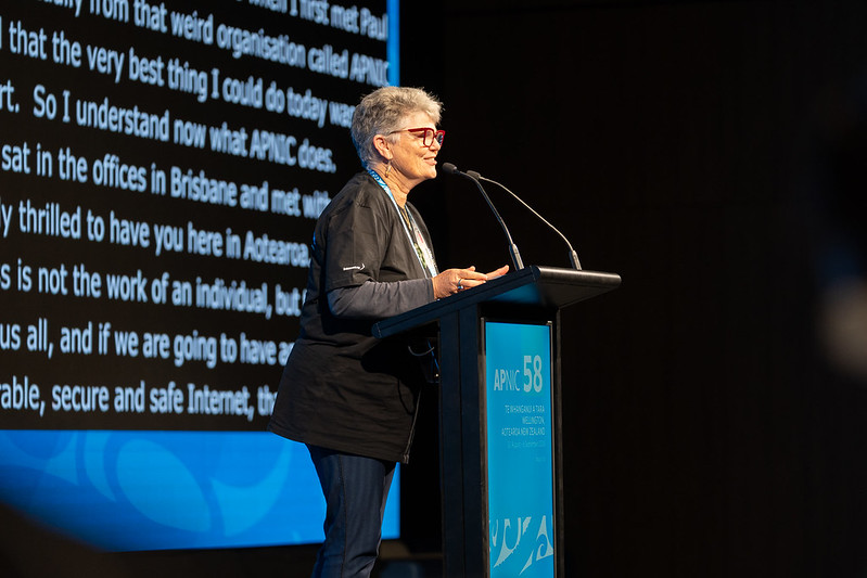A woman standing at a lectern speaking with her speech captioned on a screen behind her.
